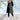 
A woman standing outdoors wearing a green long puffer coat with a detachable hood. The coat features a sleek design with long sleeves and a defined waistline. She appears happy and the coat provides a stylish, warm appearance suitable for cold weather.