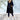 
A black women's long puffer coat with a detachable hood, showcased in a 3XL size. The coat features a sleek design with a full-length style covering down to the knees, long sleeves, and a defined waist. The model is standing, highlighting the coat's fit and structure.