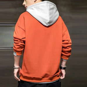 
A model wearing a burnt orange and gray dual-tone men's streetwear hoodie, showcasing the garment's distinct collar and long sleeves. The hoodie is designed with a relaxed fit, suitable for casual or sportswear settings.