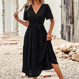 Black burnt orange midi dress with a ruffle skirt and flutter sleeves, modeled by a person wearing sunglasses with black hair.