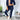 Business casual women's outfit featuring a dark blue taupe blazer and brown trousers, paired with white sneakers. The model stands near a flowerpot, highlighting the fashion-forward and stylish elements of the ensemble.