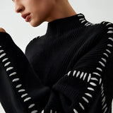 A woman wearing a chic black cut-out sweater, showcasing designer knitwear with a focus on the shoulders and neckline.