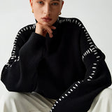Chic black cut-out sweater showcasing intricate designer knitwear, worn by a woman with shoulder-length hair, highlighting the shoulder and sleeve details in a fashion-forward style.