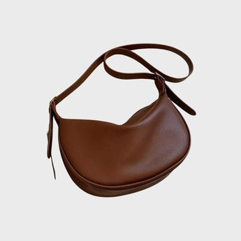Chic brown leather designer saddle bag with a luxury equestrian crossbody style, featuring a curved silhouette and adjustable shoulder strap.