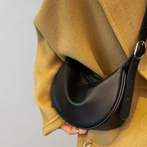 Black leather saddle bag with a minimalist design, featuring a sleek crossbody strap and luxurious craftsmanship. The bag exudes an equestrian-inspired style, combining fashion and functionality.