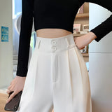 A woman wearing white wide-leg trousers, a white cropped tank top, and a grey cardigan.