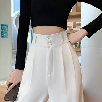 A woman wearing white wide-leg trousers, a white cropped tank top, and a grey cardigan.
