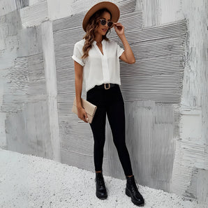 A stylish woman wearing a white blouse, black jeans, black boots, a black hat, and sunglasses.