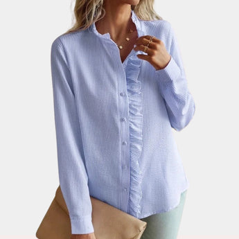 A stylish woman wearing a chic white long sleeve ruffle button-up blouse, showcasing elegant ruffles around the buttons and cuffs. The blouse fits snugly on her shoulders and arms, highlighting the sophisticated design suited for formal or casual settings.