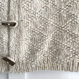 Chunky cable knit vest with wool toggle button, featuring a grey patterned textile design.