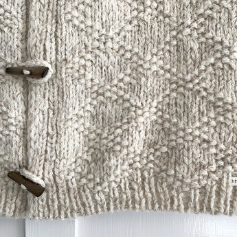 Chunky cable knit vest with wool toggle button, featuring a grey patterned textile design.
