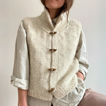 Chunky cable knit vest with wool toggle buttons, shown in XXL size, layered over a white dress shirt with a collar and sleeves, showcasing a fashionable and creative design.