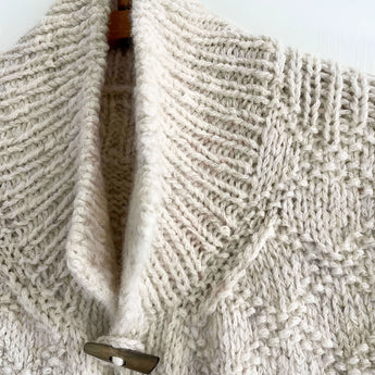 Chunky cable knit vest in beige with wool toggle buttons, featuring a textured woolen pattern.