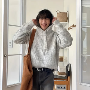 Chunky knit oversized gray hoodie worn by a person, showcasing its unisex design and cozy winter appeal. The image captures a sense of comfort, with visible details like the hoodie’s sleeves and collar.