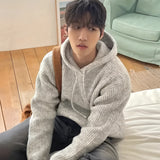 Oversized gray hoodie with a chunky knit design, suitable for winter wear, featuring long sleeves and a relaxed fit, designed for unisex use, with a person sitting while wearing it.