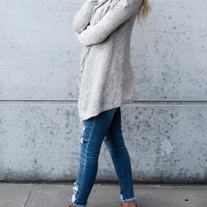Woman wearing a chunky turtleneck sweater paired with taupe ankle boots, showcasing winter knitwear fashion. The sweater has long sleeves and a loose fit, styled with grey tones.