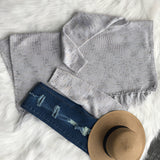 
A woman wearing a chunky turtleneck sweater paired with taupe ankle boots. She is holding a bag and appears to be standing on a wooden surface. The sweater features a textured knit design with long sleeves, and she is also wearing denim jeans. The color scheme includes shades of grey and taupe.