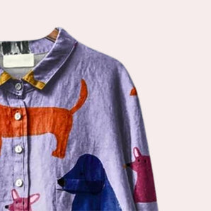 A colorful dog print shirt with an artistic design, displayed on a clothes hanger. The shirt features a vibrant electric blue background, short sleeves, and a classic collar, showcasing a playful pattern ideal for casual pet lovers.