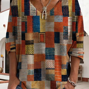 A colorful geometric bohemian V-neck blouse with tribal patterns, featuring vibrant orange and white designs, showcased on a model from the shoulders down, emphasizing the fashion-forward style and textile details.