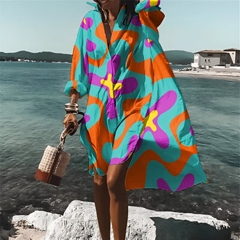 Colorful retro print kaftan cover-up in vibrant psychedelic patterns, featuring long sleeves, worn by a person on a beach. The kaftan flows with shades of blue and pink, suitable as a stylish beachwear option. The scene includes water and sky in the background, enhancing the summery vibe.
