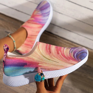 Colorful women's slip-on walking sneakers with a rainbow mesh design, featuring lightweight materials. The sneakers are showcased on a model wearing a pink dress, highlighting the vibrant colors of the shoes.