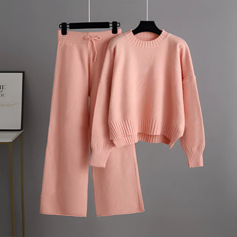 A pink, cozy cream knit sweater and wide-leg pants set on a clothes hanger, featuring a round neck, long sleeves, and a relaxed fit, ideal for winter loungewear.