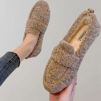 Light grey cozy fleece slippers for women, featuring a soft plush design and an anti-slip sole. The image shows a close-up view of the slippers, highlighting their snug interior and fashionably simple pattern. A hand is visible, possibly adjusting the slipper.