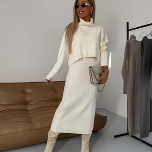 Cream knit turtleneck midi dress with long sleeves, shown in a beige color, styled for winter fashion. The dress features a fitted waist, and the model is standing, showcasing the elegant design.