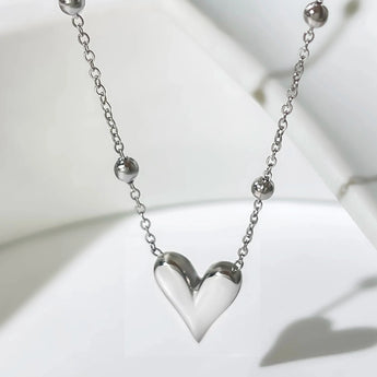A dainty silver heart pendant necklace on a delicate chain, displayed against a neutral background, highlighting its elegant and romantic design.