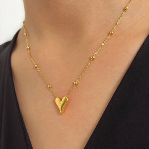 A hand holding an elegant 18K gold heart pendant necklace around the neck, showcasing its dainty, romantic design.