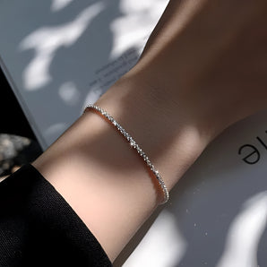 A woman wearing a dainty diamond bracelet on her wrist, showcasing the elegant minimalist silver bridal jewelry against a backdrop of a formal dress.