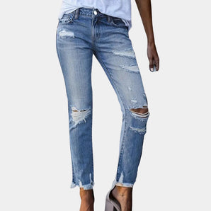 Women's light wash denim distressed ripped skinny jeans featuring a fitted silhouette with visible rips and frayed hems, styled with white shoes and a blue tartan-patterned top, highlighting the knee and leg areas.
