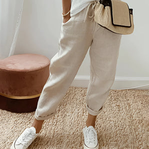 A beige eco-friendly compact woven crossbody bag, designed as a neutral travel purse in size 3XL, shown hanging against a neutral background.