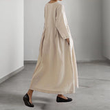 Eco-friendly oatmeal linen maxi dress with a minimalist loose fit, featuring long sleeves and a flowing silhouette. The dress is displayed in an indoor setting, showcasing its elegant simplicity and natural texture.