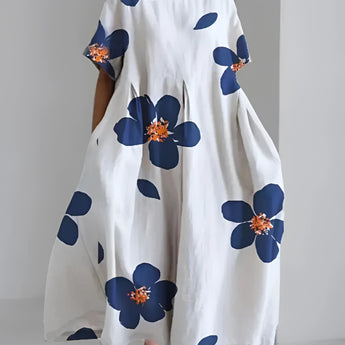 
An eco-friendly oversized floral dress featuring a white fabric with a green leaf print, displayed in a Blu color variant, size 4XL. The dress showcases a loose fit with a round neckline and long sleeves, set against a neutral background.