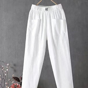 Eco-friendly white linen pants with an elastic waist and lightweight fit, displayed on a clothes hanger against a soft, natural backdrop with plants and curtains.