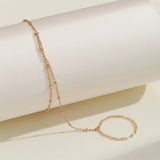Elegant adjustable gold chain bracelet with minimalist circle charm, displayed on a beige surface with natural twig accents.