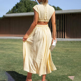 Elegant black midi dress with a back cutout, showcasing evening wear style; the dress features short sleeves and a fitted waist, worn by a person standing on grass.