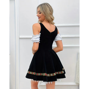 Elegant black velvet skater dress with backless design, embroidered hem, and white cuffs worn by a woman.