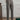 Elegant beige high-waisted pleated trousers for women, shown in a charcoal gray variant, suitable for office wear. The image focuses on the waist and leg areas, highlighting the neat pleats and tailored fit. The trousers are paired with a dress shirt, adding to the professional look.