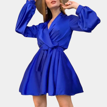 Elegant blue satin wrap dress with long sleeves, modeled by a person standing, showcasing the dress's waist tie and mini length.