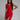 
Woman wearing an elegant red cocktail dress with a sleeveless V-neck wrap design, knee-length cut, smiling and posing with one hand on her waist.
