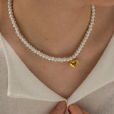 A woman's hand gently touching her neck, wearing an elegant bridal pearl choker with a gold heart charm.
