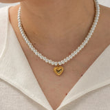 Elegant bridal pearl choker with gold heart charm worn around the neck of a woman.
