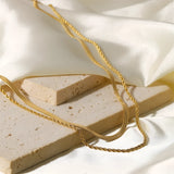 Elegant double layered gold necklace displayed on a beige background, highlighting its minimalist and delicate design.