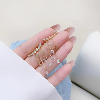 Elegant gold chain drop earrings with crystal star charms displayed on a model's ear, highlighting the jewelry's delicate and stylish design.