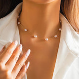 Close-up of a woman wearing an elegant gold chain pearl necklace, highlighting the intricate design on her neck and collar area.