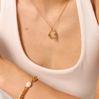 Elegant gold necklace with mother of pearl sunburst pendant, featuring Hamsa and celestial charms, worn on a woman's neck.
