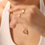 Elegant gold necklace featuring a mother of pearl sunburst pendant with Hamsa and celestial charms, displayed on a neck.