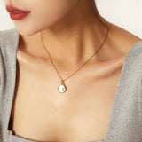Elegant gold necklace with a mother of pearl sunburst pendant, featuring Hamsa and celestial charms, worn on a woman's neck.